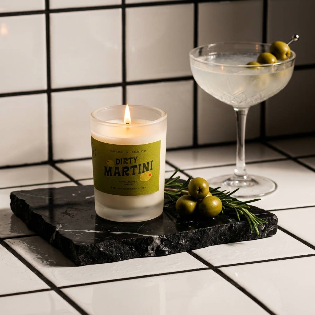 Candle labeled 'Dirty Martini' on a black marble tray with a cocktail glass and olives in the background.